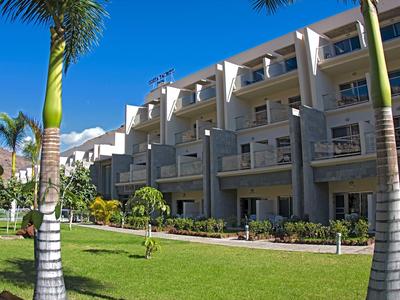 Modern hotel complex with balconies and well-maintained lawn under a blue sky.