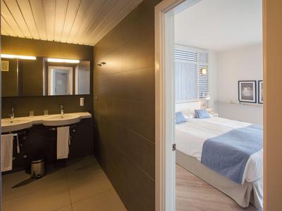Innenansicht mit Blick vom Badezimmer in ein helles Schlafzimmer mit weißen und blauen Bettdecken.