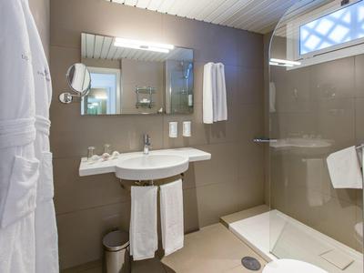Modernes Bad mit weißem Waschbecken, großer Spiegel, Dusche mit Glaswand und beigen Fliesen.