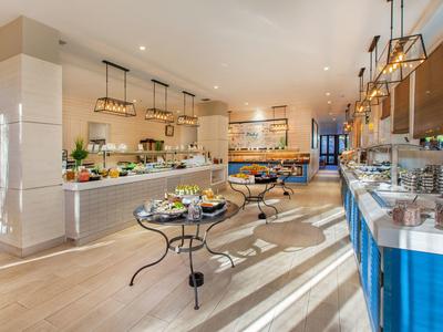 Hell eingerichteter Frühstücksraum mit Buffet, Esstischen und modernen Leuchten, heller Holzboden.
