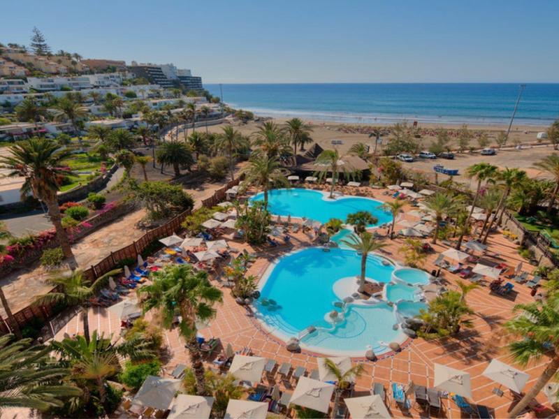 Resort con più piscine, palme, lettini, vicino a una spiaggia sabbiosa e all'oceano.