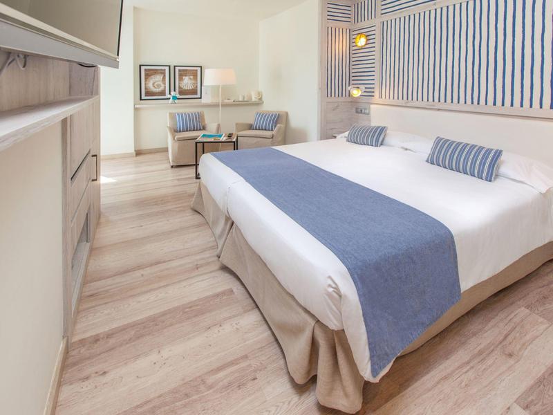 Camera d'hotel luminosa con letto grande, accenti blu, zona salotto e pavimento in legno.