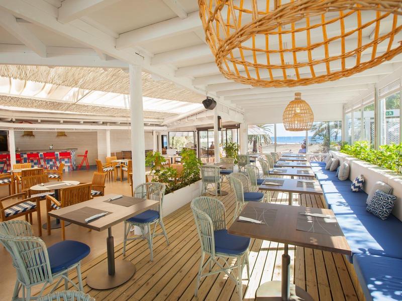 Ristorante all'aperto con pavimento in legno, sedie miste, tavoli e lampade sospese sotto un tetto bianco.