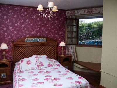 Schlafzimmer mit Holzmöbeln, Doppelbett, Blumenbettwäsche und offenem Fenster mit Blick nach draußen.