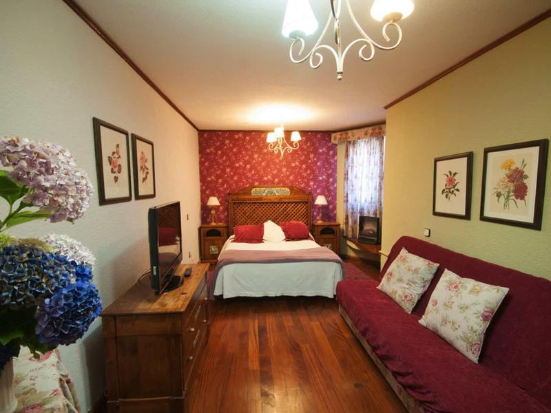 Gemütliches Schlafzimmer mit Holzboden, Doppelbett, rotem Sofa und Blumendekor an den Wänden.