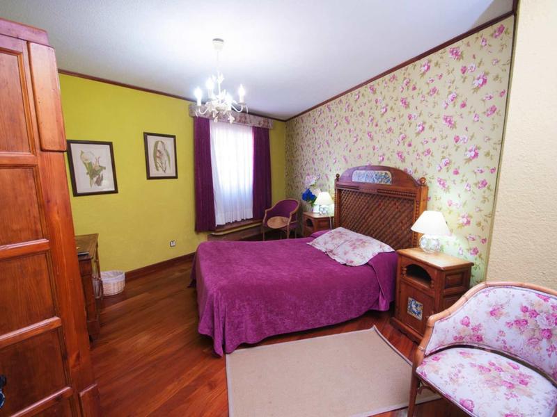 Gemütliches Schlafzimmer mit Holzboden, lila Bettdecke, Blumen-Tapete und antiken Möbeln.