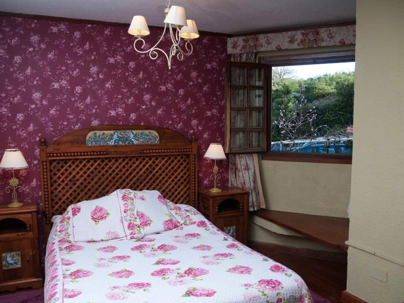 Schlafzimmer mit Holzmöbeln, Doppelbett, Blumenbettwäsche und offenem Fenster mit Blick nach draußen.
