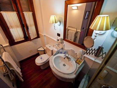 Piccolo bagno con lavabo, bidet, WC e specchio su pavimento in legno scuro.