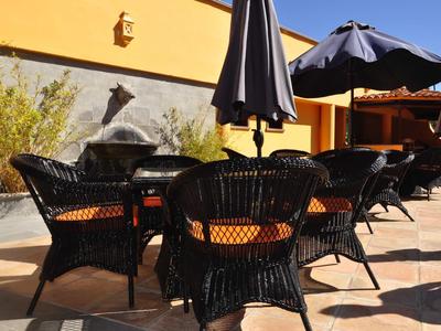 Terrasse avec chaises en osier noir et parasols devant un mur jaune.