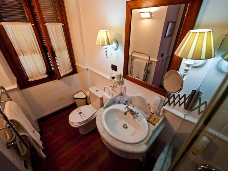 Piccolo bagno con lavabo, bidet, WC e specchio su pavimento in legno scuro.