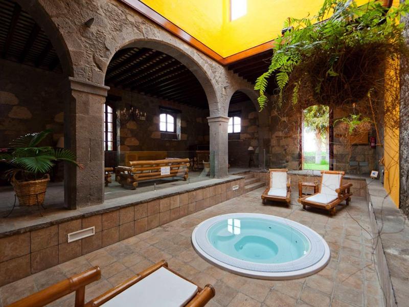 Vasca idromassaggio interna in un elegante spa con archi in pietra e lettini.