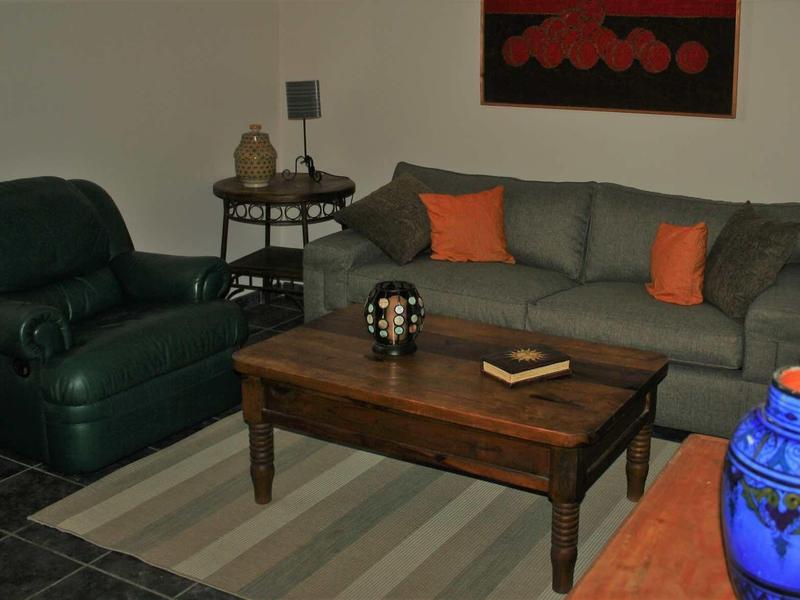 Gezellig zithoekje met grijze bank, groene fauteuil en rustieke houten tafel in een hotelkamer.