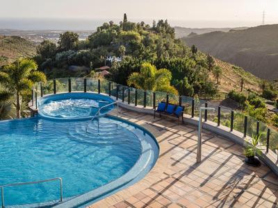 Piscina con vasca idromassaggio e area salotto su una terrazza con vista su paesaggio collinare e mare.