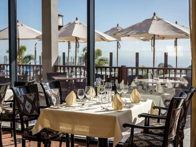 Tavolo apparecchiato su terrazza con vista sul mare e ombrelloni.