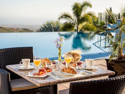 Tavolo con colazione e bevande accanto a una piscina con palme sullo sfondo.