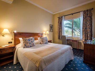 Camera d'hotel accogliente con letto matrimoniale, comodini e vista sulle palme dalla finestra.