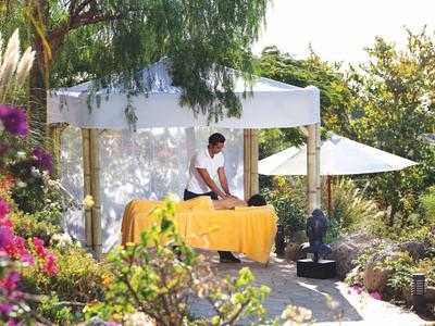 Massaggio rilassante sotto una tettoia bianca in un giardino lussureggiante con sole.