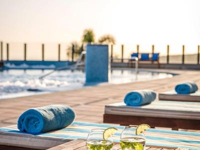 Area piscina con lettini prendisole e asciugamani blu, tavolo con bevande al tramonto.