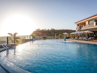Grande piscina all'aperto con terrazza solarium e edificio dell'hotel al tramonto.