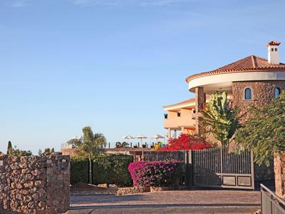 Grande casa con tetto rosso dietro un cancello in pietra e cespugli di bouganville in fiore