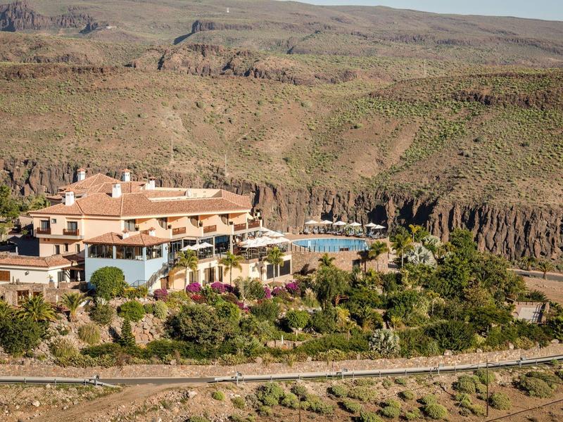 Hotel in paesaggio montano con piscina e vegetazione circostante.