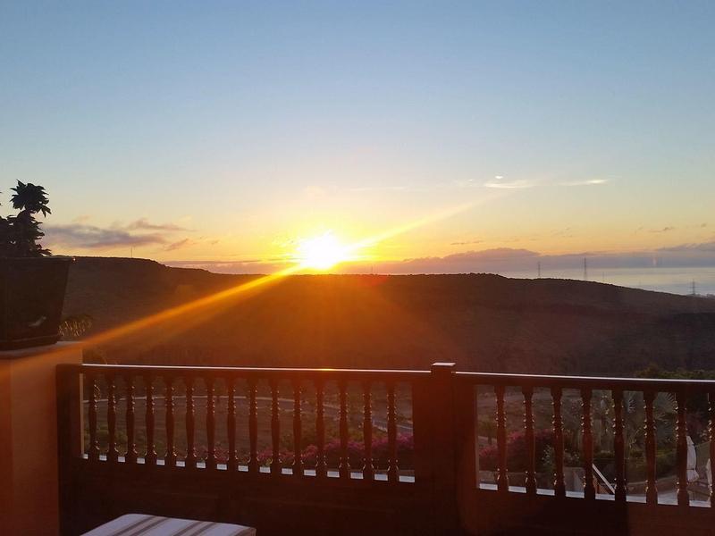 Tramonto su una terrazza con ringhiera in legno e due piante in vaso.
