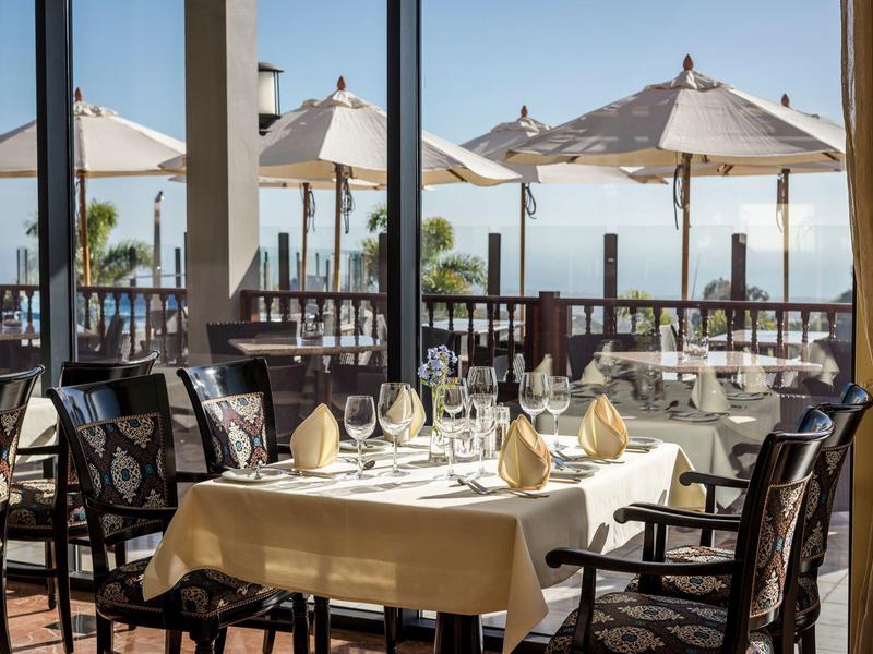 Tavolo apparecchiato su terrazza con vista sul mare e ombrelloni.