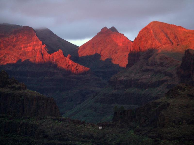 Cime montuose rosse al tramonto su una valle scura con nuvole