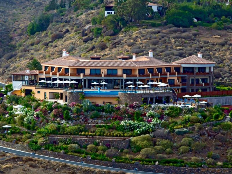 Grande hotel in collina con vegetazione mediterranea e vista panoramica.