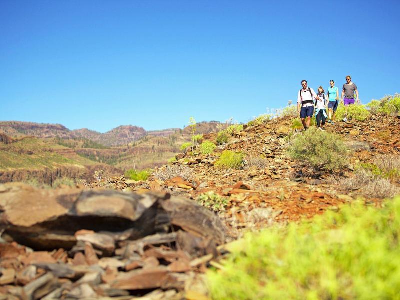 Tre escursionisti su una collina rocciosa sotto un cielo azzurro limpido.