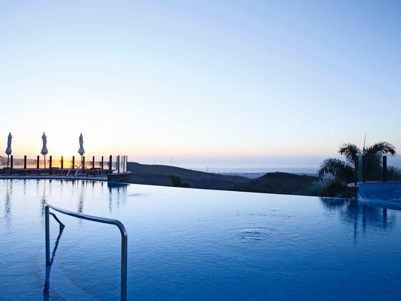 Piscina a sfioro che si affaccia su colline al crepuscolo con ombrelli chiusi