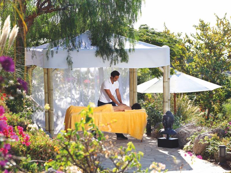 Massaggio rilassante sotto una tettoia bianca in un giardino lussureggiante con sole.