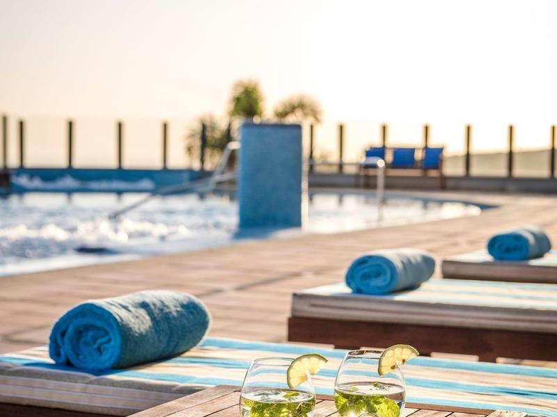 Area piscina con lettini prendisole e asciugamani blu, tavolo con bevande al tramonto.