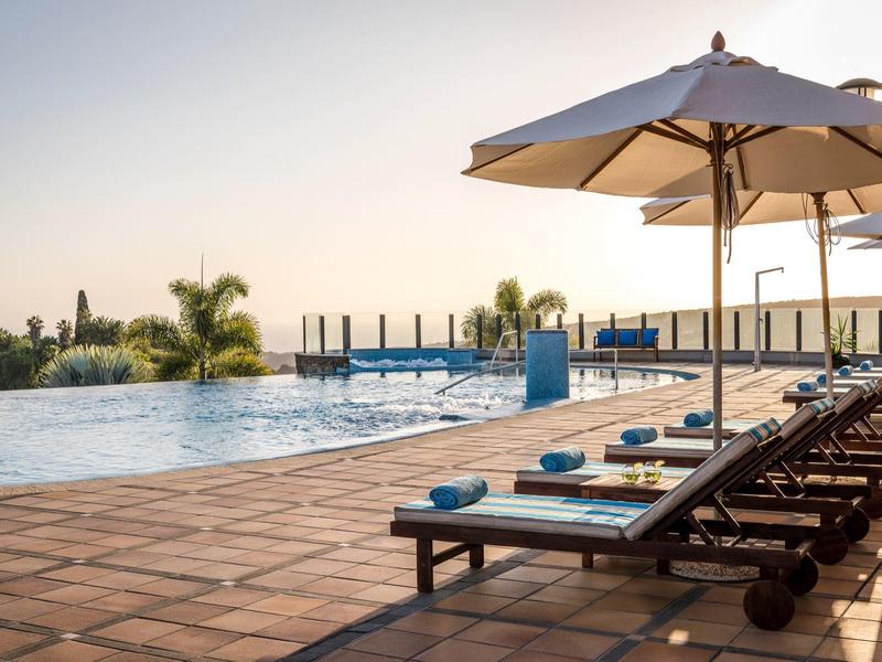 Area piscina dell'hotel con lettini e ombrelloni al tramonto.