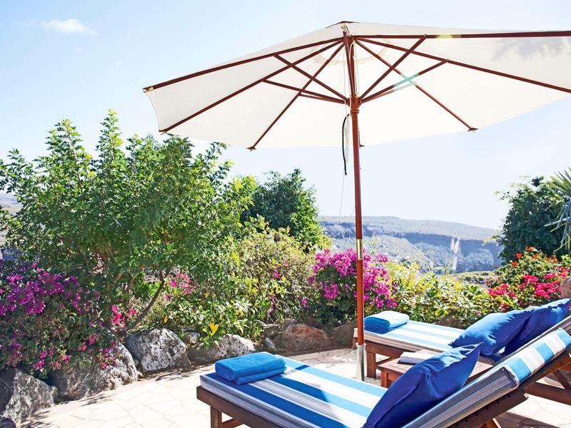 Vista di lettini e ombrellone in un giardino fiorito con vista panoramica.