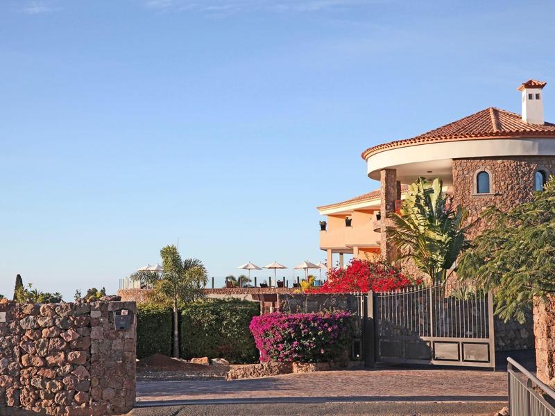 Grande casa con tetto rosso dietro un cancello in pietra e cespugli di bouganville in fiore