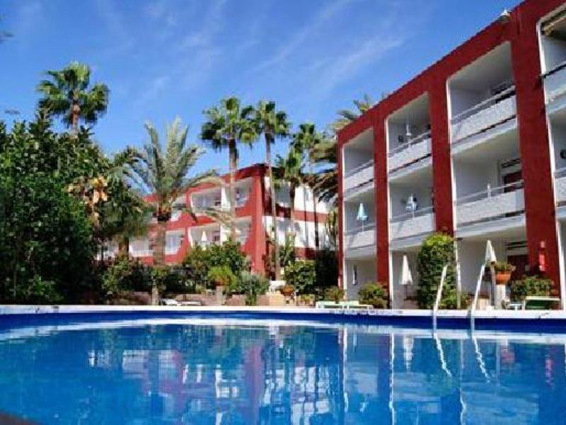 Complexe hôtelier avec piscine entourée de palmiers et de bâtiments rouges sous un ciel bleu.