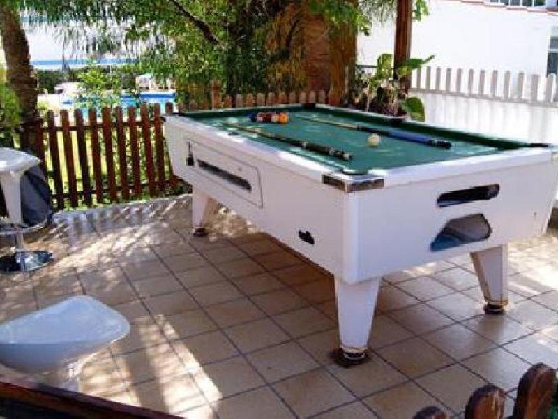 Une table de billard blanche sur une terrasse carrelée avec des sièges et des plantes vertes en arrière-plan.