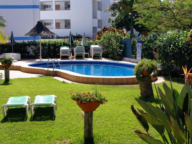 Espace piscine avec chaises longues et jardin luxuriant devant un bâtiment hôtelier