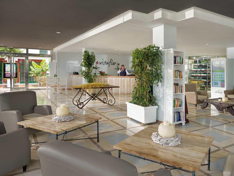 Heller Empfangsbereich mit Holztischen, Pflanzen, moderner Einrichtung und bequemen Sesseln.