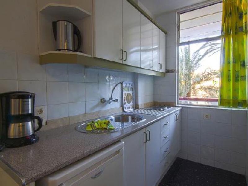 Cuisine compacte avec cafetière, évier et fenêtre avec rideau vert.