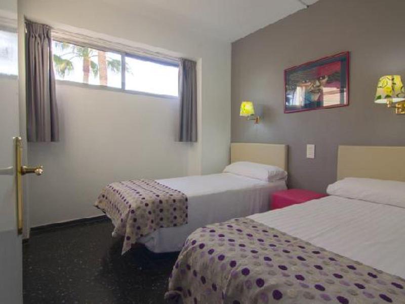 Une chambre simple avec deux lits simples, des murs gris et une petite fenêtre.