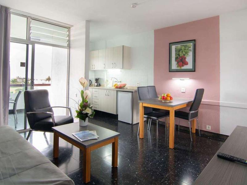 Salon moderne avec canapé, table à manger, kitchenette et grande fenêtre.