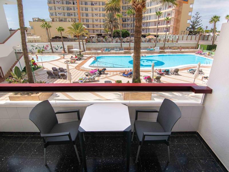 Balcon avec table et deux chaises avec vue sur piscine et bâtiments de l'hôtel.