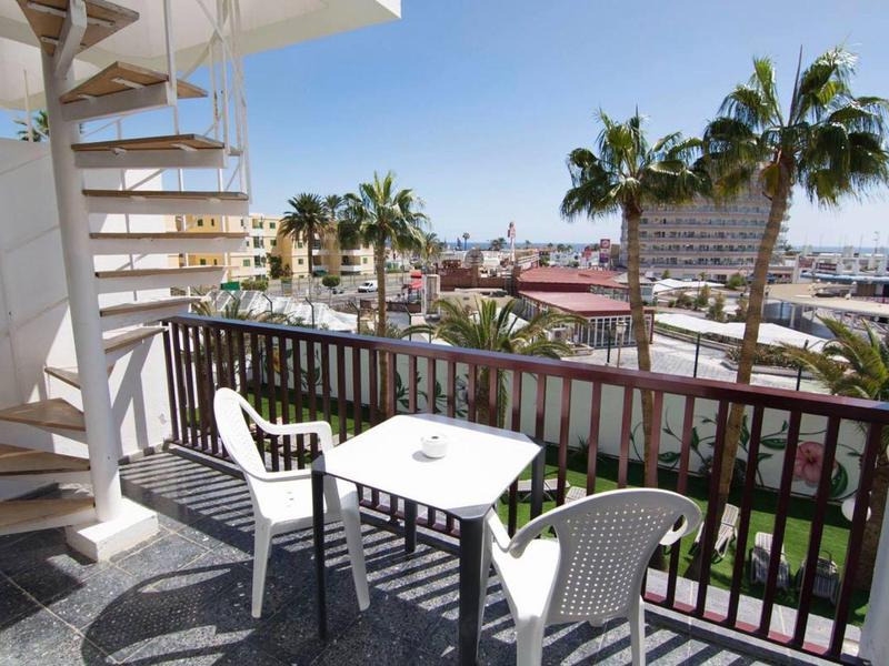 Balcon avec table blanche et deux chaises, vue sur les palmiers et le port sous un ciel clair