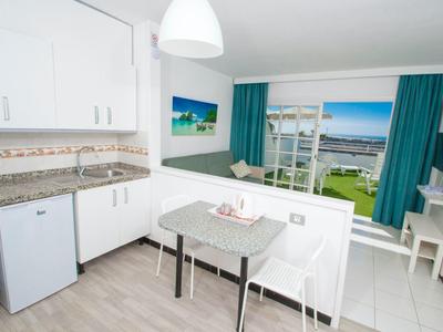 Helle Küchenzeile mit Tisch und Stühlen, Aussicht auf Balkon und Meer durch große Fenster.