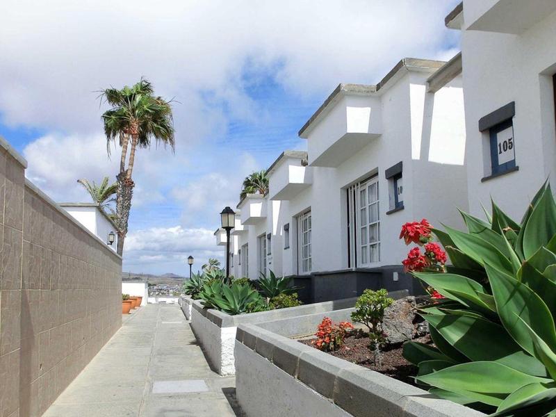 Weiße Häuserreihe mit Fensterläden, Palmen und Blumentopf mit roten Blumen in sonniger Straße.