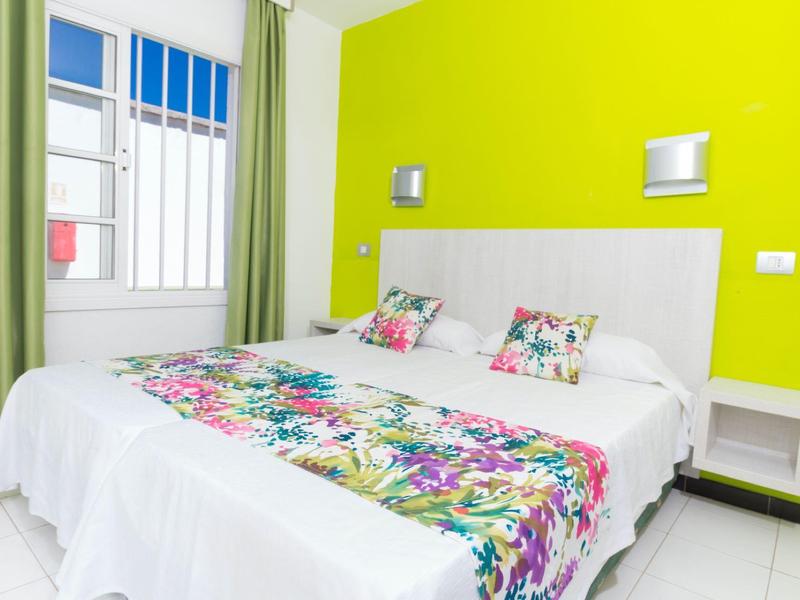 Hellgrünes Schlafzimmer mit großem Bett, weißen Möbeln und bunten Blumendekorationen am Kopfteil.