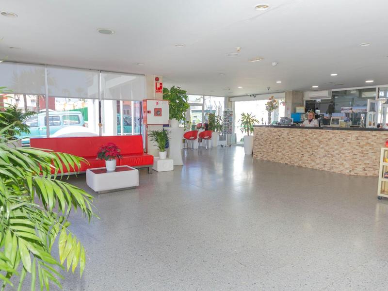 Helle, offene Empfangshalle mit roten Sofas, Pflanzen und hellem Bodenbelag.