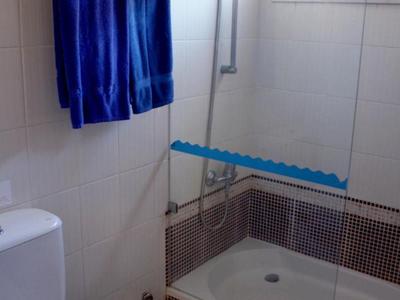 Kompaktní koupelna se sprchou, toaletou, modrými ručníky a malou stoličkou.